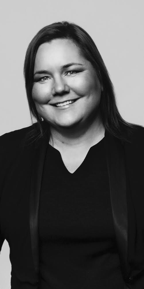 Portret uśmiechniętej kobiety w czarnej marynarce na jasnym tle, zdjęcie czarno-białe.