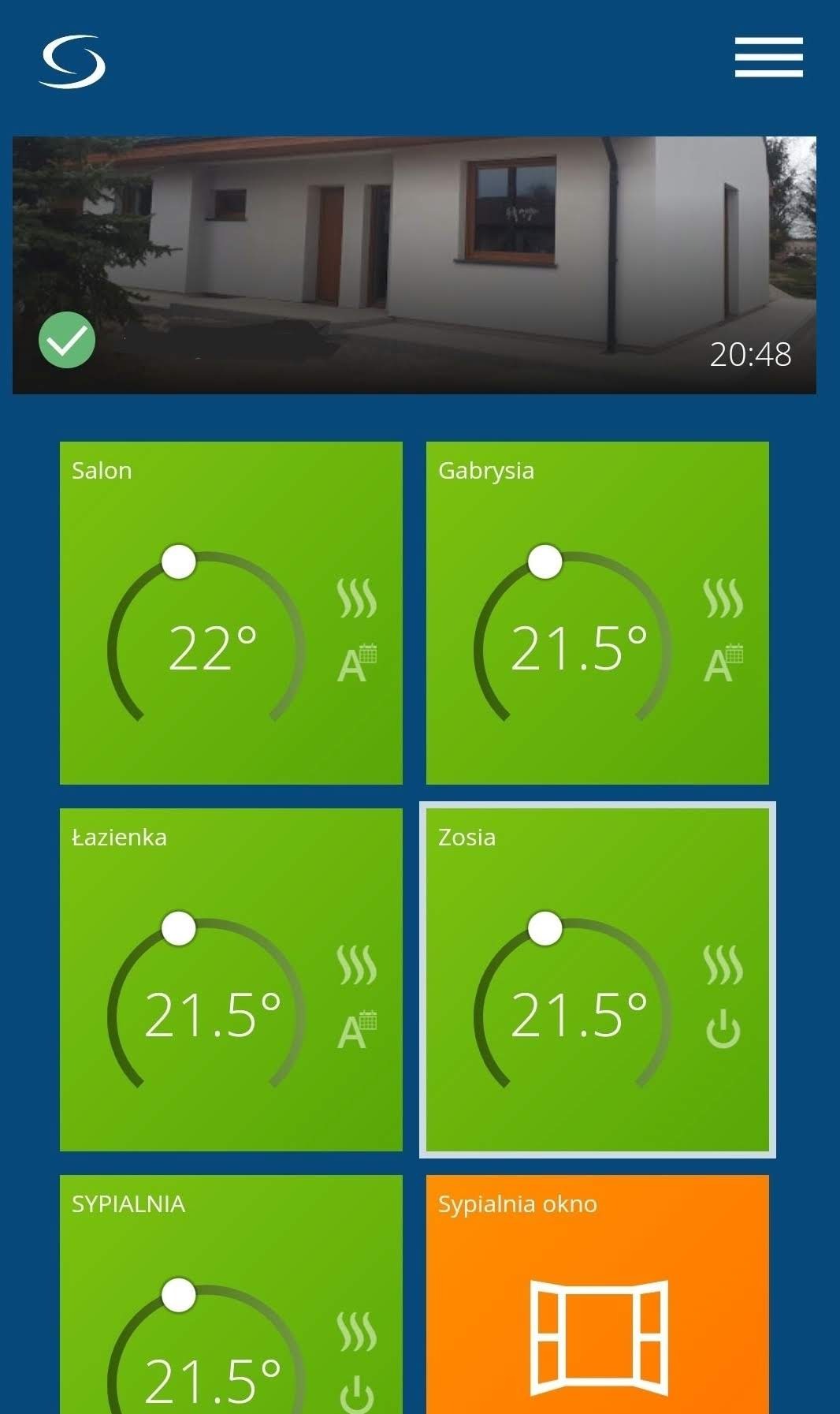 Ekran aplikacji mobilnej do zarządzania temperaturą w domu, z widokiem na budynek w tle i ustawieniami dla poszczególnych pomieszczeń: salon, Gabrysia, łazienka, Zosia, sypialnia.