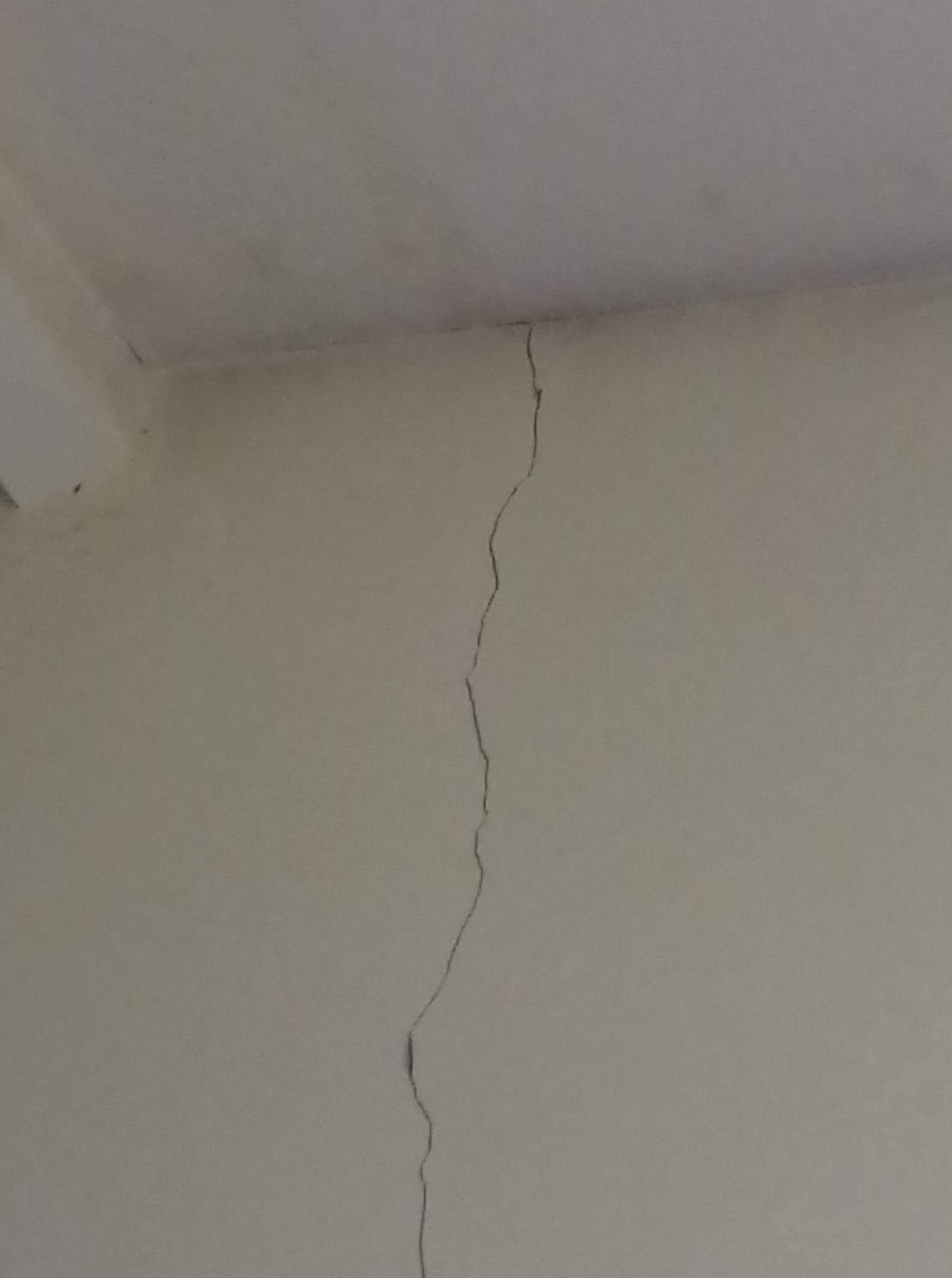 Pęknięcie na ścianie, biegnące od sufitu w dół, widoczne na gładkiej, pomalowanej powierzchni.
