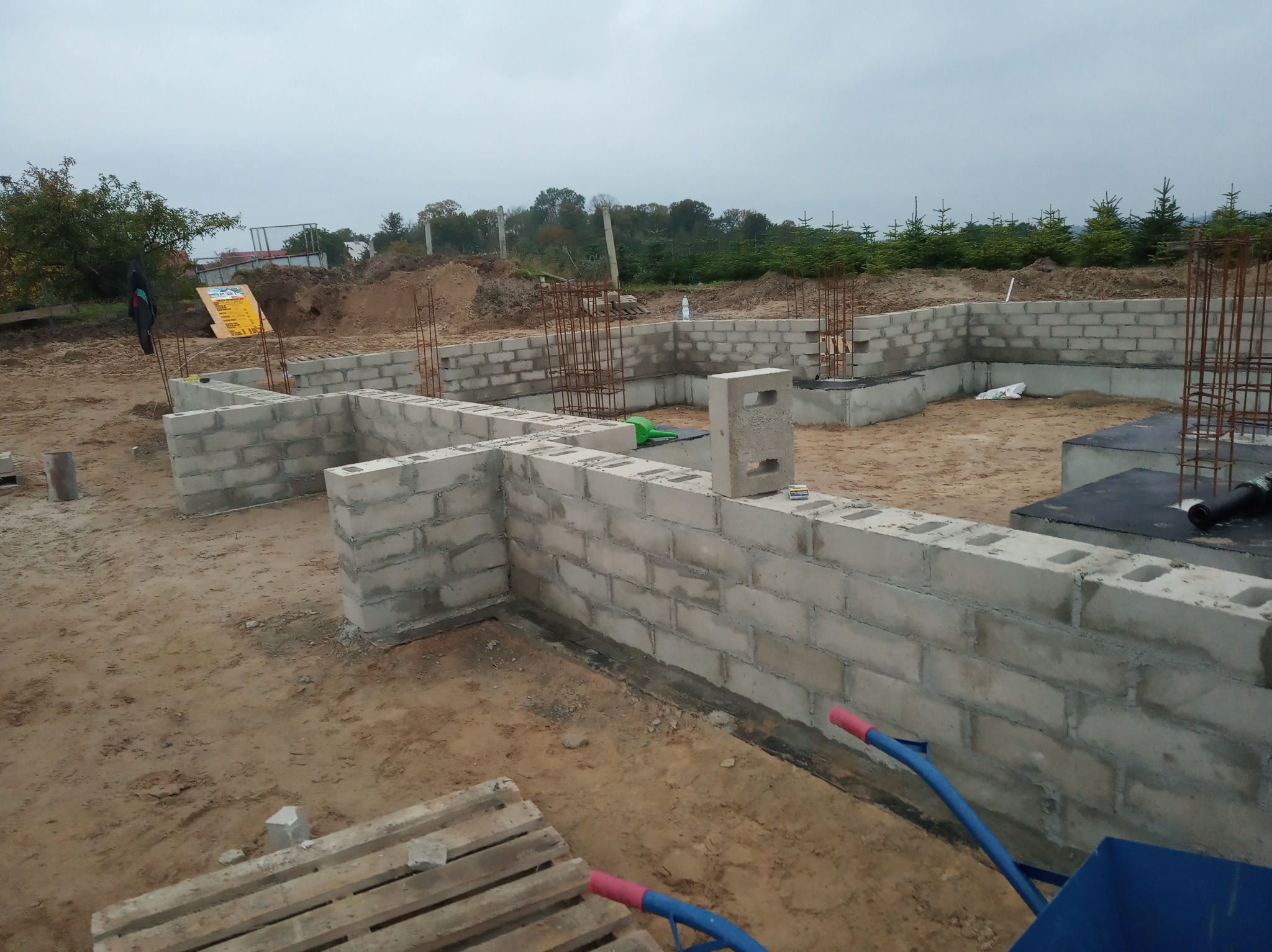 Wznoszenie ścian fundamentowych z bloczków betonowych na budowie w Szczecinie, widoczne zbrojenia pionowe i częściowa izolacja.