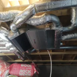 Centralna jednostka klimatyzacji kanałowej marki Gree, z podłączonymi izolowanymi przewodami wentylacyjnymi, zamontowana pod drewnianym stropem, z widoczną izolacją Rockwool w tle.