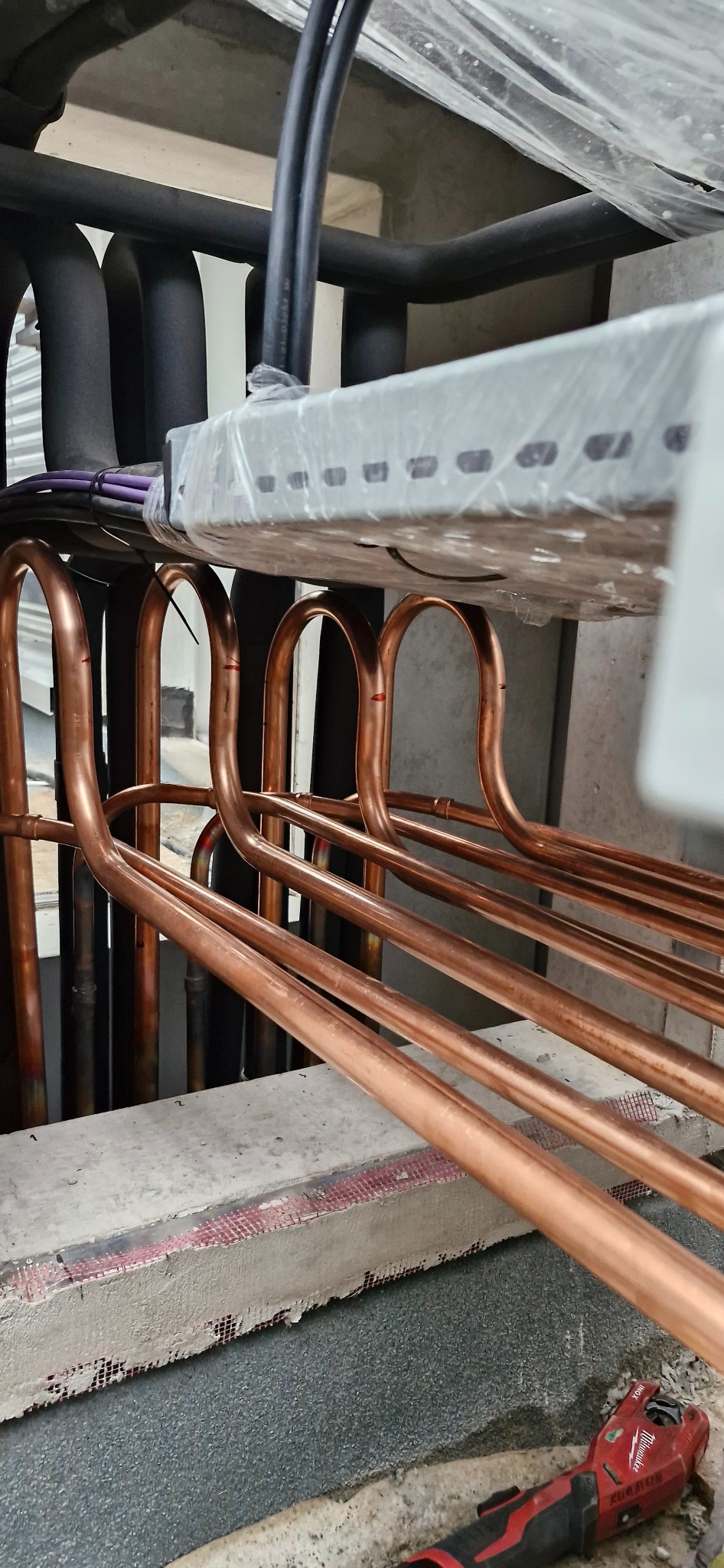 Miedziane rury klimatyzacji, widoczne narzędzie do cięcia rur. Elementy instalacji w trakcie montażu. Detal techniczny, instalacja w budynku.