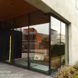 Nowoczesne, duże przeszklenie w domu z betonu architektonicznego, widoczna drabina przy ścianie i odbicie sąsiedniego budynku w szybach.