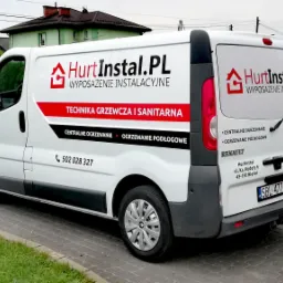 Oklejony biały van Renault Trafic firmy HurtInstal.pl z wyposażeniem instalacyjnym, techniką grzewczą i sanitarną, centralnym ogrzewaniem i ogrzewaniem podłogowym, zaparkowany na brukowanej ulicy...