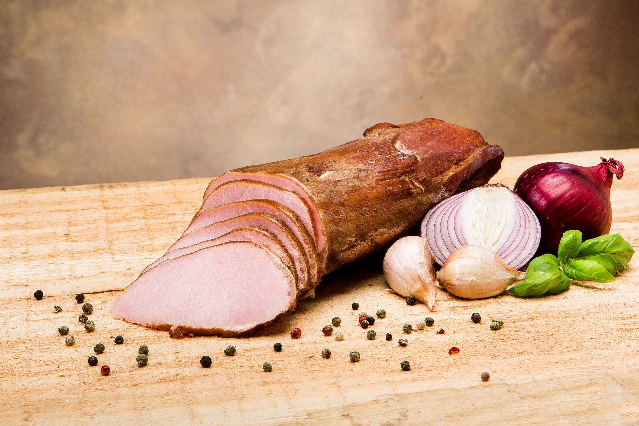 Kompozycja z wędzonki, pokrojonej w plastry, z główkami czosnku, przekrojoną i całą czerwoną cebulą, listkami bazylii i ziarnami pieprzu na drewnianej desce.