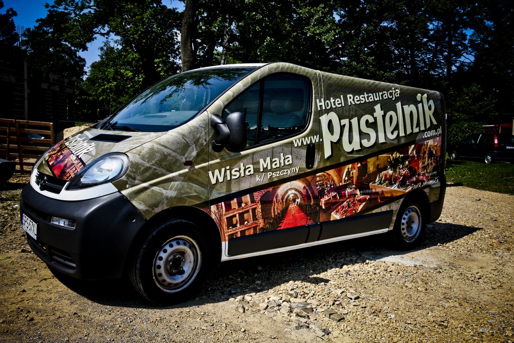 Oklejony bus Hotelu Restauracji Pustelnik z Wisły Małej, z grafiką przedstawiającą wnętrze restauracji, zaparkowany na żwirowym podłożu.