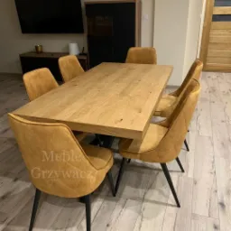 Drewniany st&oacute;ł jadalny z sześcioma tapicerowanymi krzesłami w kolorze musztardowym, ustawiony w nowoczesnym wnętrzu z drewnianą podłogą i szafką RTV w tle.