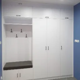 Biała zabudowa meblowa z siedziskiem i wieszakami w przedpokoju, minimalistyczny design, niebieska ściana w tle.