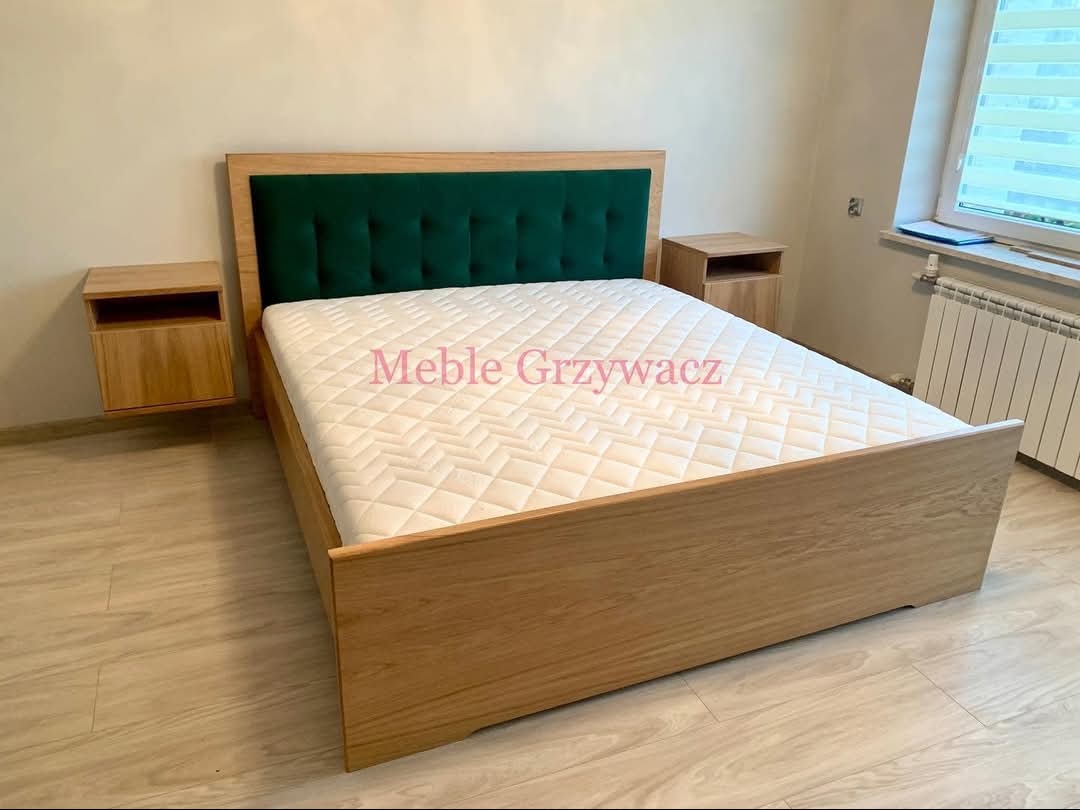 Drewniane łóżko z zielonym wezgłowiem i szafkami nocnymi, minimalistyczny design, jasna podłoga, widok z boku.