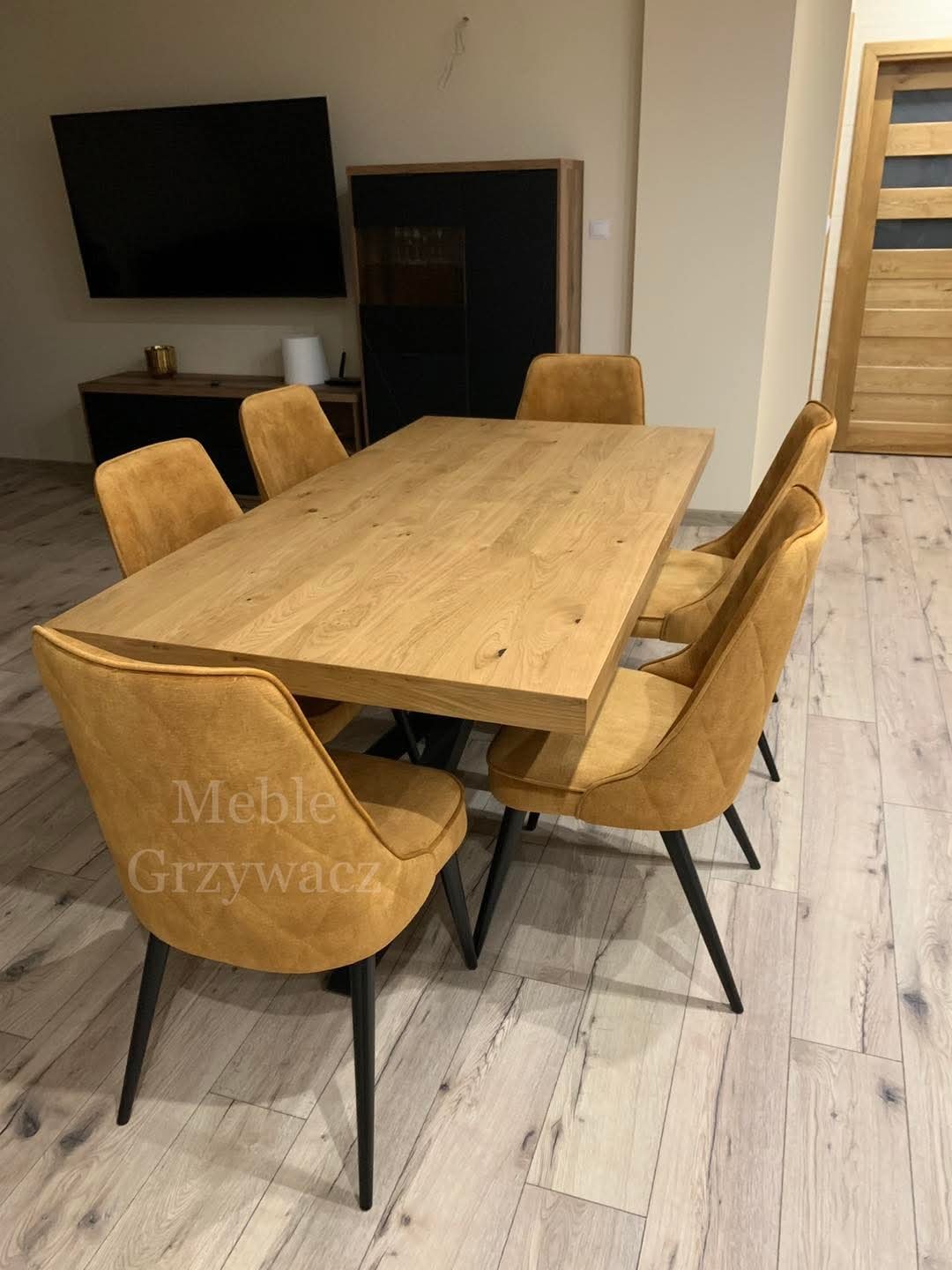 Drewniany stół jadalny z sześcioma tapicerowanymi krzesłami w kolorze musztardowym, ustawiony w nowoczesnym wnętrzu z drewnianą podłogą i szafką RTV w tle.