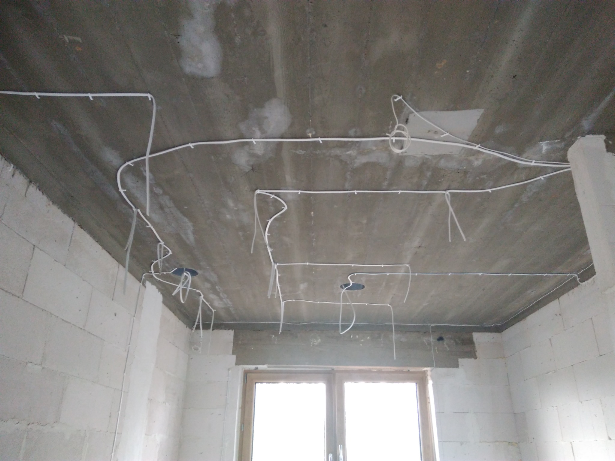 Surowy betonowy sufit z widocznym okablowaniem elektrycznym w białych rurkach, w nowym budynku z pustaków.