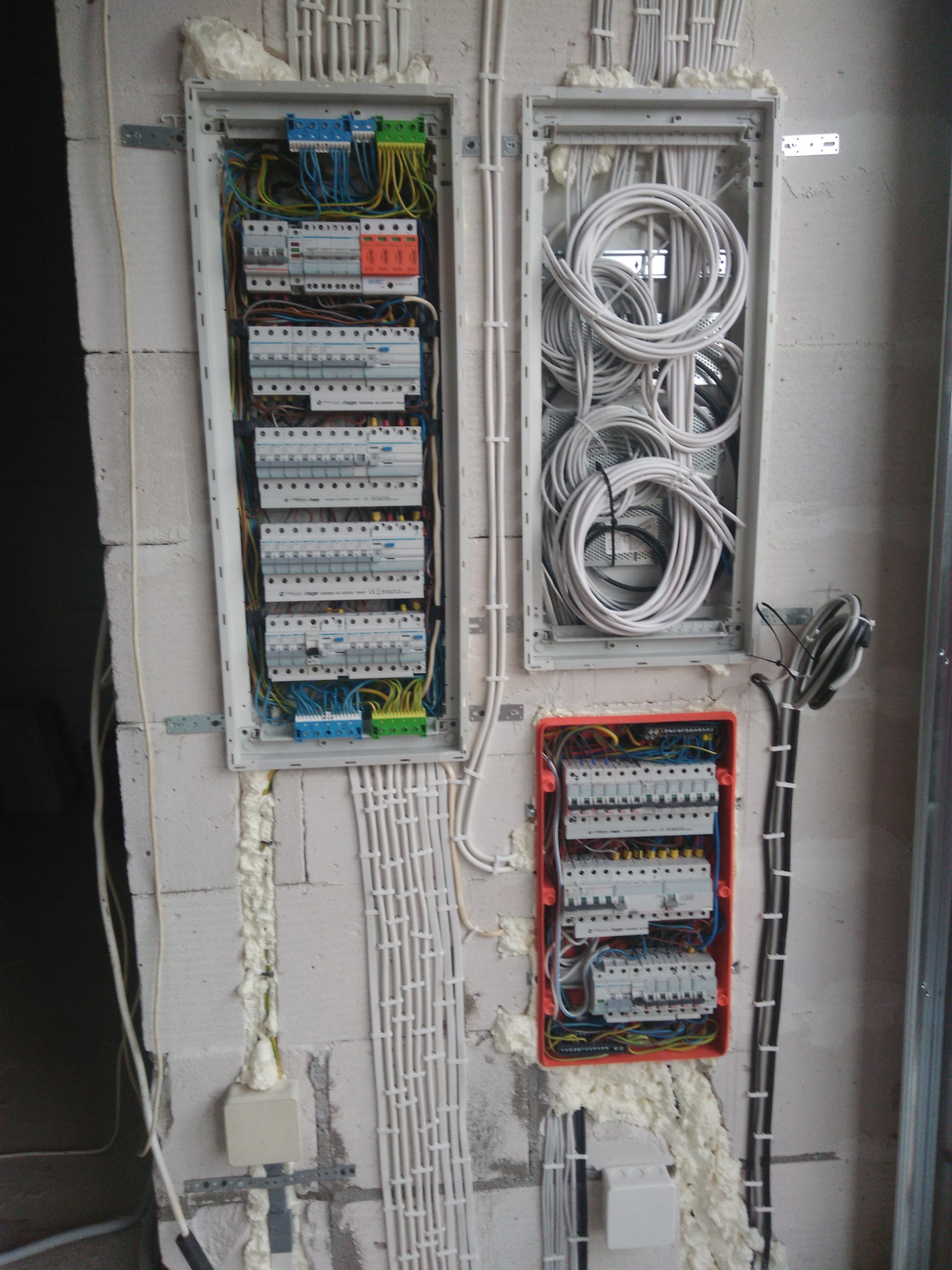 Trzy skrzynki elektryczne zamontowane na ścianie z betonu komórkowego, z widocznymi przewodami, bezpiecznikami i pianką montażową.