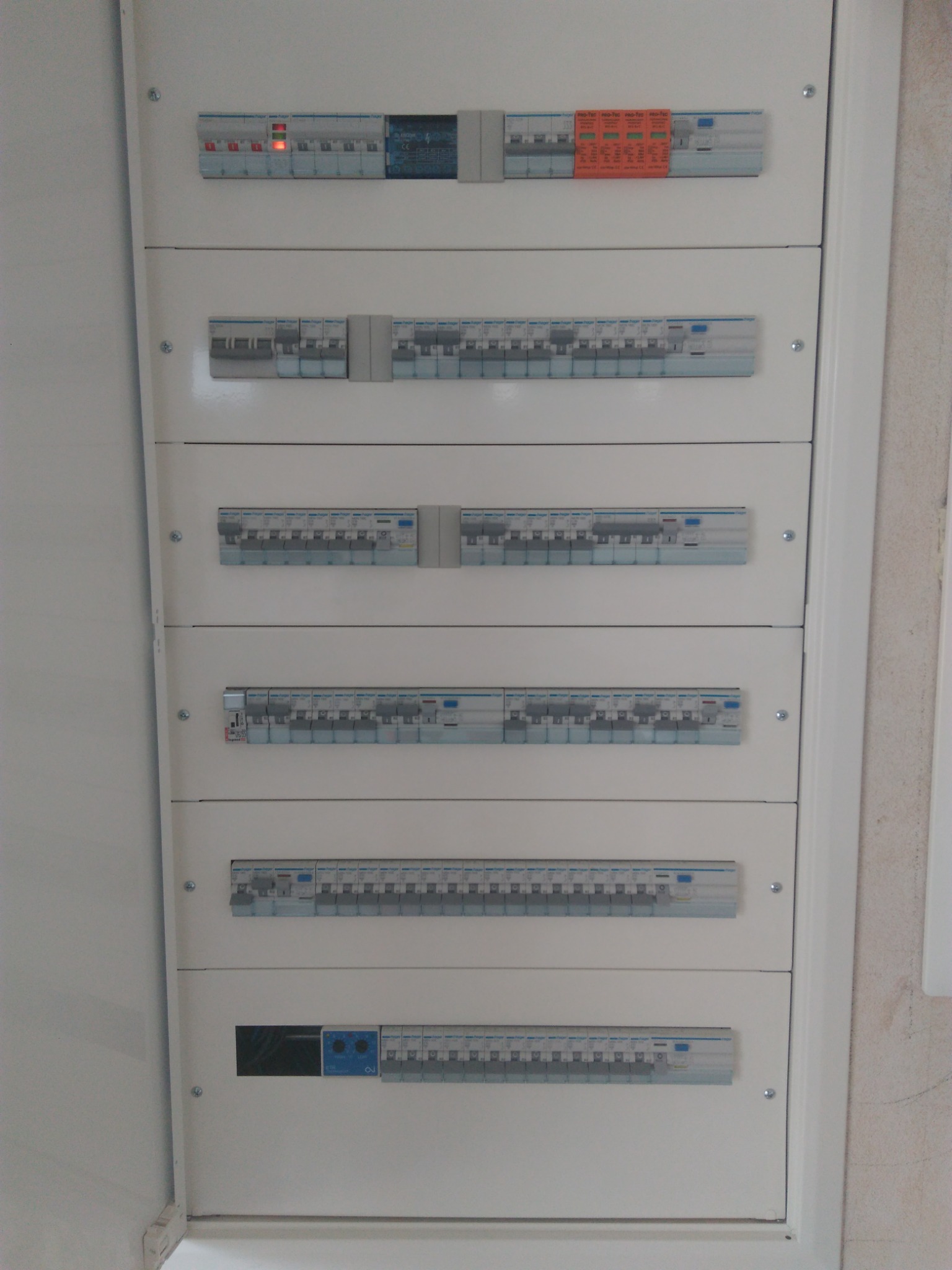 Rozdzielnica elektryczna z wieloma zabezpieczeniami nadprądowymi i różnicowoprądowymi marki Hager, umieszczona w białej obudowie, widoczne bezpieczniki z opisami.