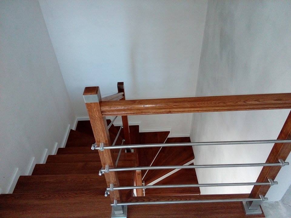 Klatka schodowa z ciemnego drewna z metalowymi poręczami, widok z góry, białe ściany.