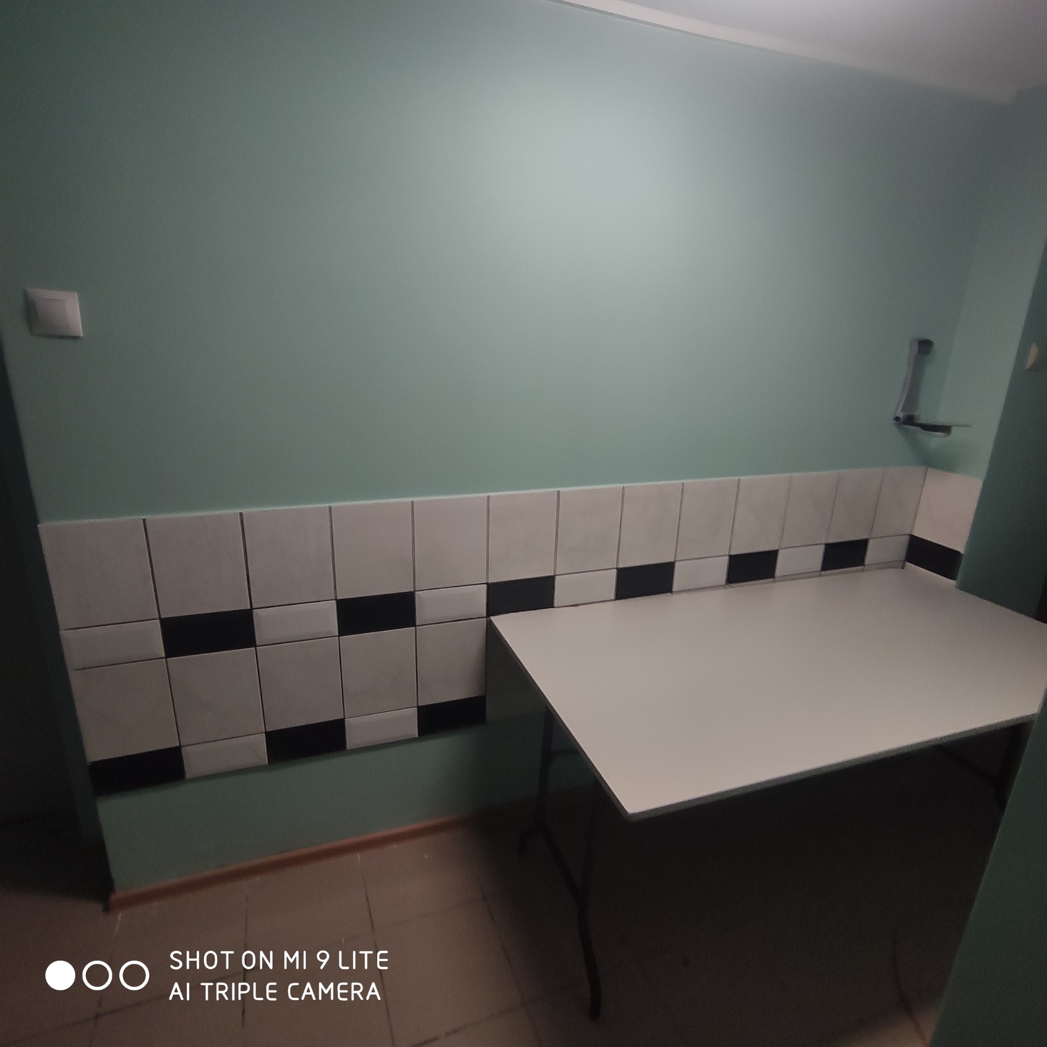 Ściana w kolorze miętowym z rzędem białych płytek z czarnymi akcentami, nad którymi widoczny jest biały stół składany.