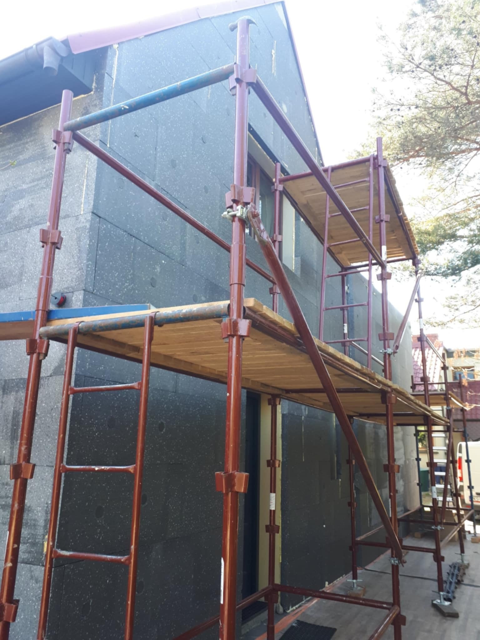 Dom w trakcie ocieplania, widoczne rusztowanie i ściana pokryta ciemnym materiałem izolacyjnym, prawdopodobnie styropianem grafitowym.