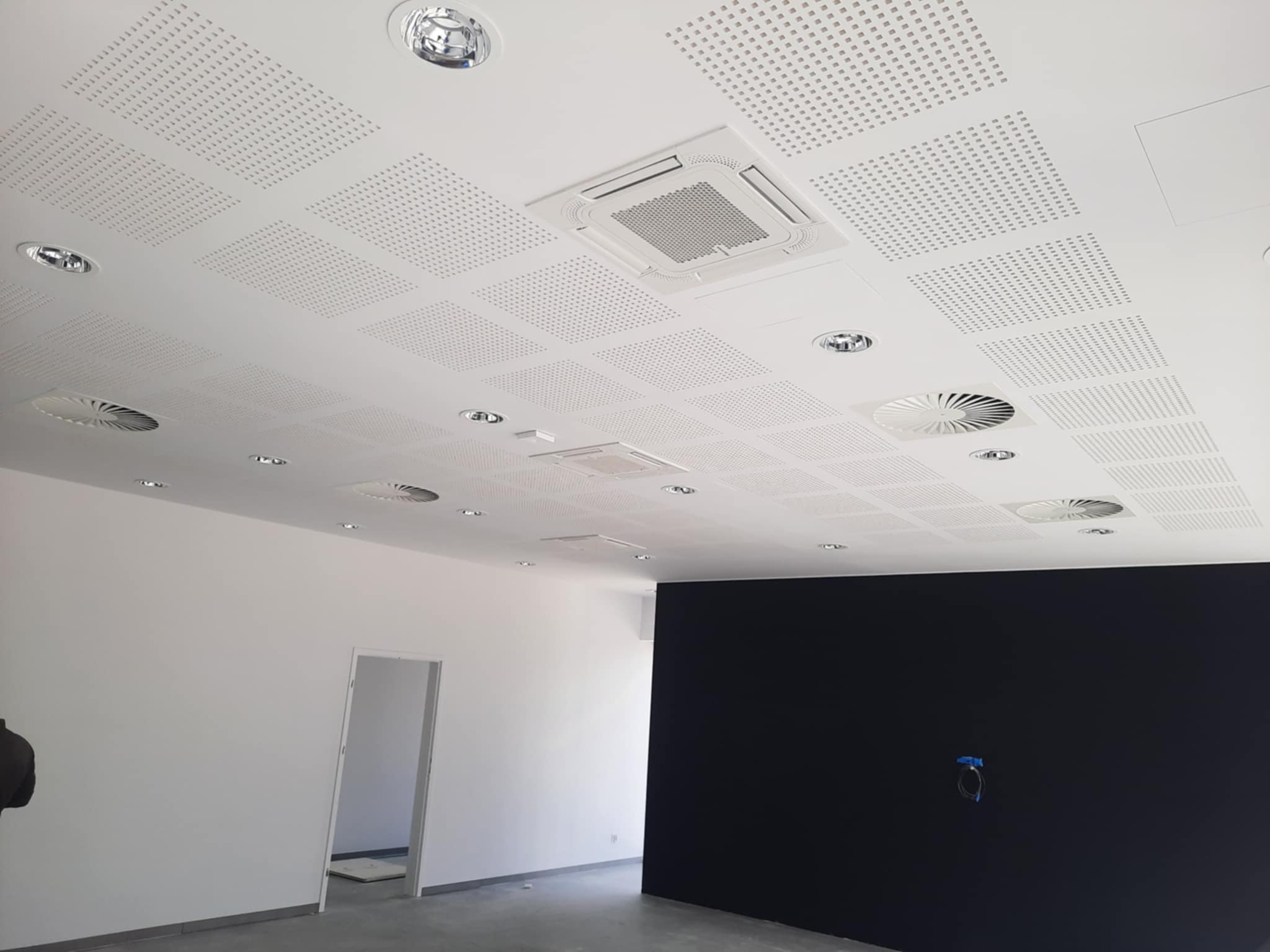 Biuro z zamontowanym podwieszanym sufitem kasetonowym z perforacją, oświetleniem punktowym i klimatyzacją centralną, ściany pomalowane na biało i czarno, widoczny fragment wejścia do innego...
