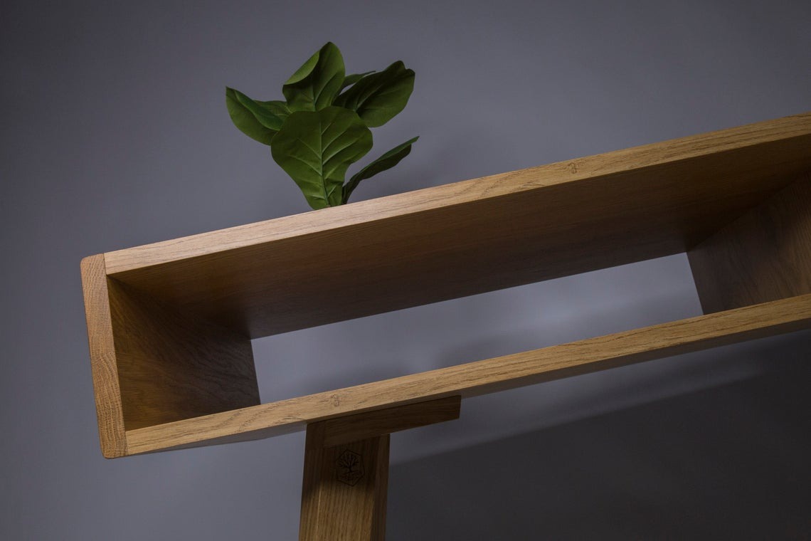 Nowoczesna, dębowa półka z geometrycznymi przegródkami, na której stoi roślina doniczkowa, z widocznym logo firmy na nodze.
