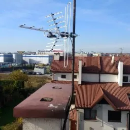 Antena telewizyjna zamontowana na kominie budynku mieszkalnego z widokiem na zabudowę miejską w tle.