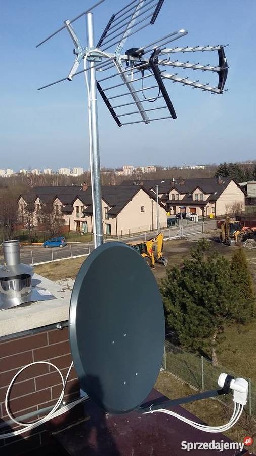 Antena satelitarna i antena naziemna zamontowane na dachu budynku z widokiem na zabudowę miejską i plac budowy w tle.