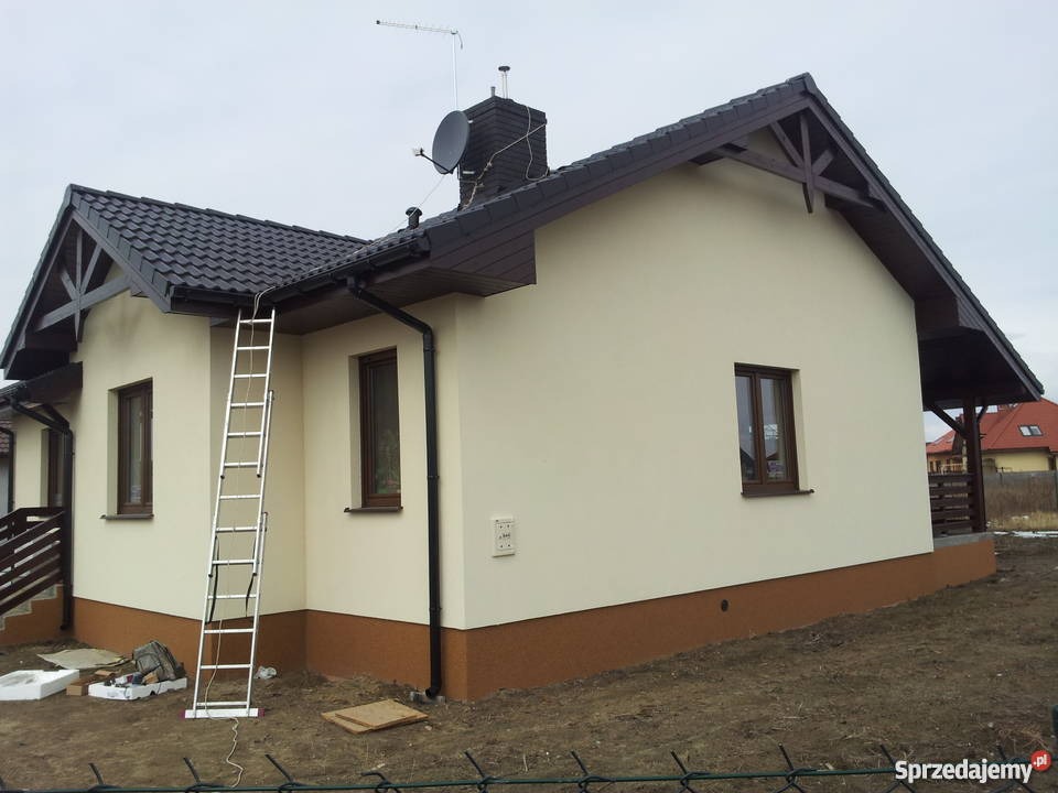 Dom jednorodzinny z anteną satelitarną i anteną naziemną na dachu, z przystawioną drabiną aluminiową, widok z zewnątrz.