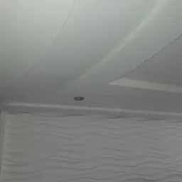 Biały sufit podwieszany z oświetleniem punktowym i dekoracyjna ściana z falistym wzorem 3D.