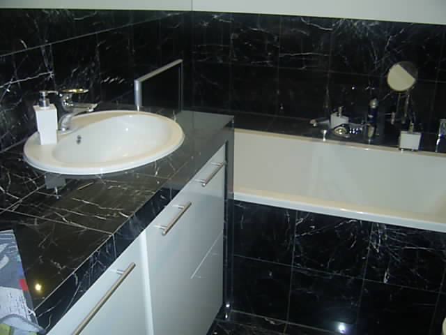 Czarno-biała łazienka z marmurowymi płytkami, biała umywalka nablatowa z armaturą i szafka z metalowymi uchwytami, wanna z akcesoriami na krawędzi.