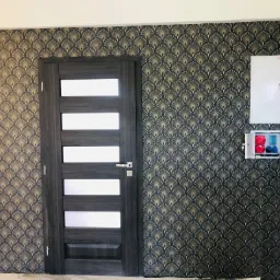 Ściana wykończona tapetą w stylu art deco z motywem wachlarzy w kolorach złota i granatu, obok ciemnoszare drzwi z przeszkleniami i biała skrzynka elektryczna.