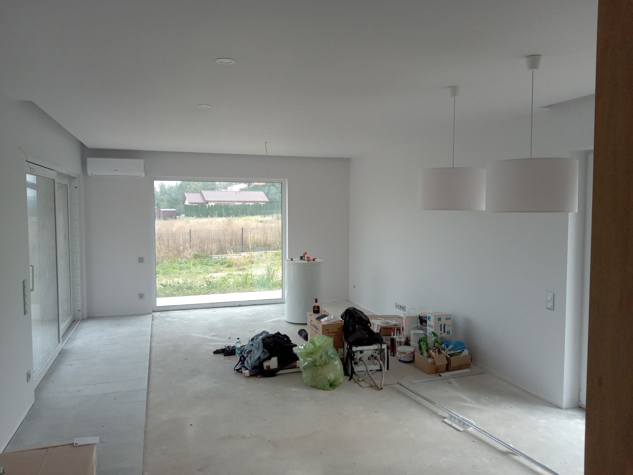 Wnętrze w stanie surowym po malowaniu ścian na biało, widoczne przygotowania do dalszych prac wykończeniowych, w tym narzędzia i materiały budowlane.