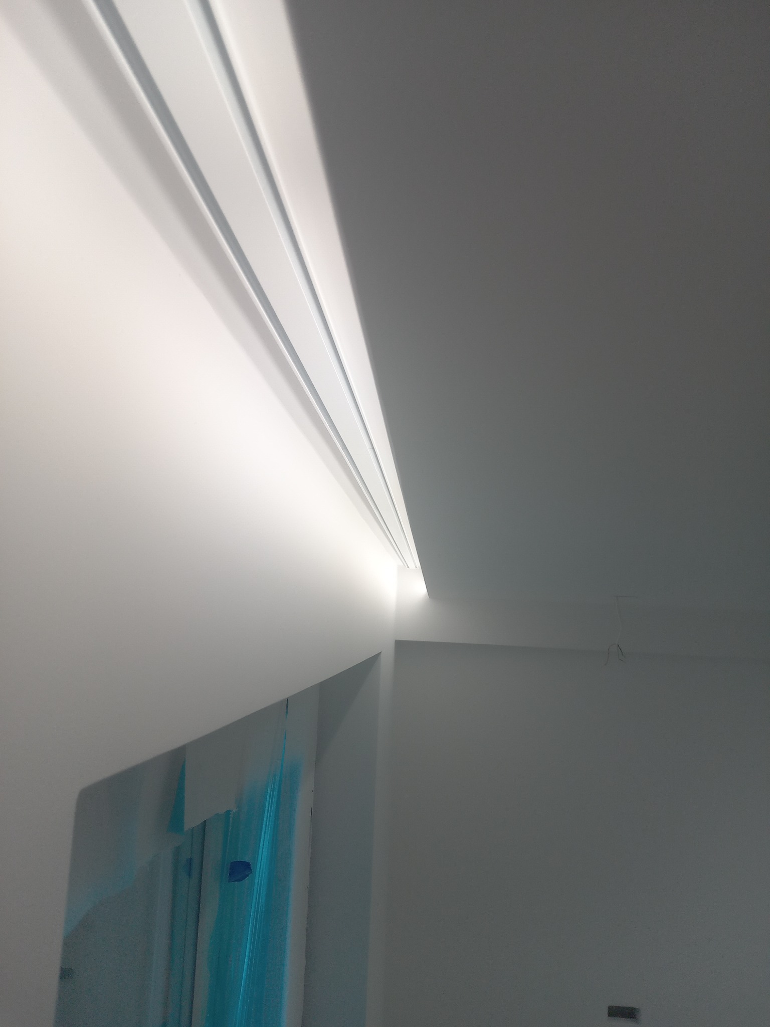 Nowoczesny, biały sufit z ukrytym oświetleniem LED w listwach, widok z dołu, fragment ściany zabezpieczony folią.