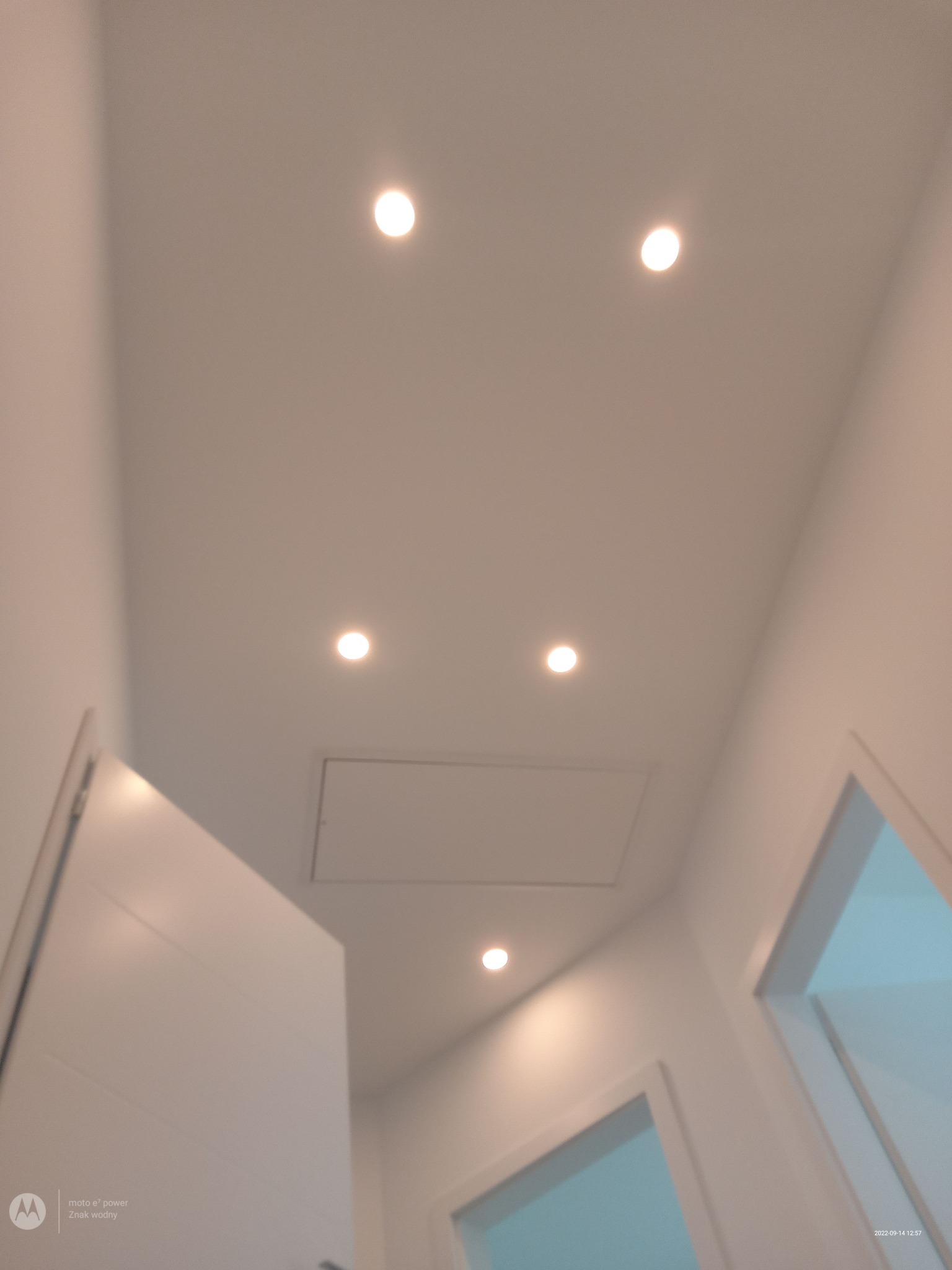 Biały sufit z równomiernie rozmieszczonymi punktowymi lampami LED i klapą rewizyjną, widok z dołu.