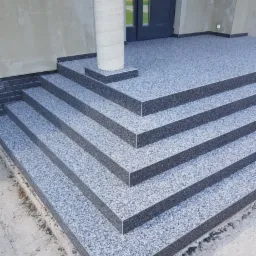 Eleganckie schody zewnętrzne z żywicy epoksydowej w odcieniach szarości, prowadzące do drzwi wejściowych. Kolumna dekoracyjna przy wejściu. Detal wykończenia.