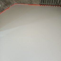 Imperial -Tim Adam Migo - Jasna, gładka posadzka z pomarańczową taśmą przy ścianie i fragmentem surowego sufitu. Minimalistyczne ujęcie, podkreślające równą powierzchnię.