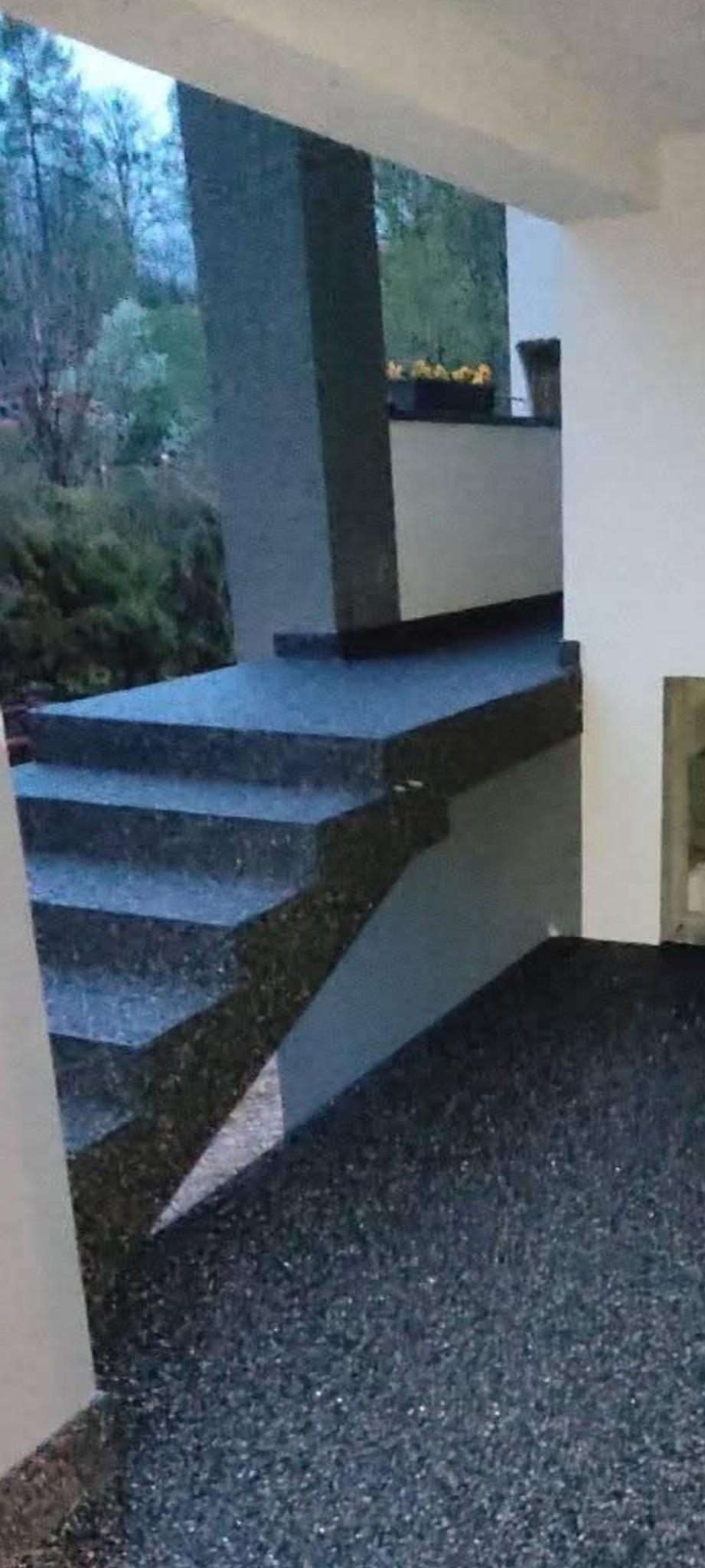 Granitowe schody zewnętrzne z żywiczną posadzką, widok z dołu. Na górze widać rośliny w donicach. Tło stanowią drzewa.