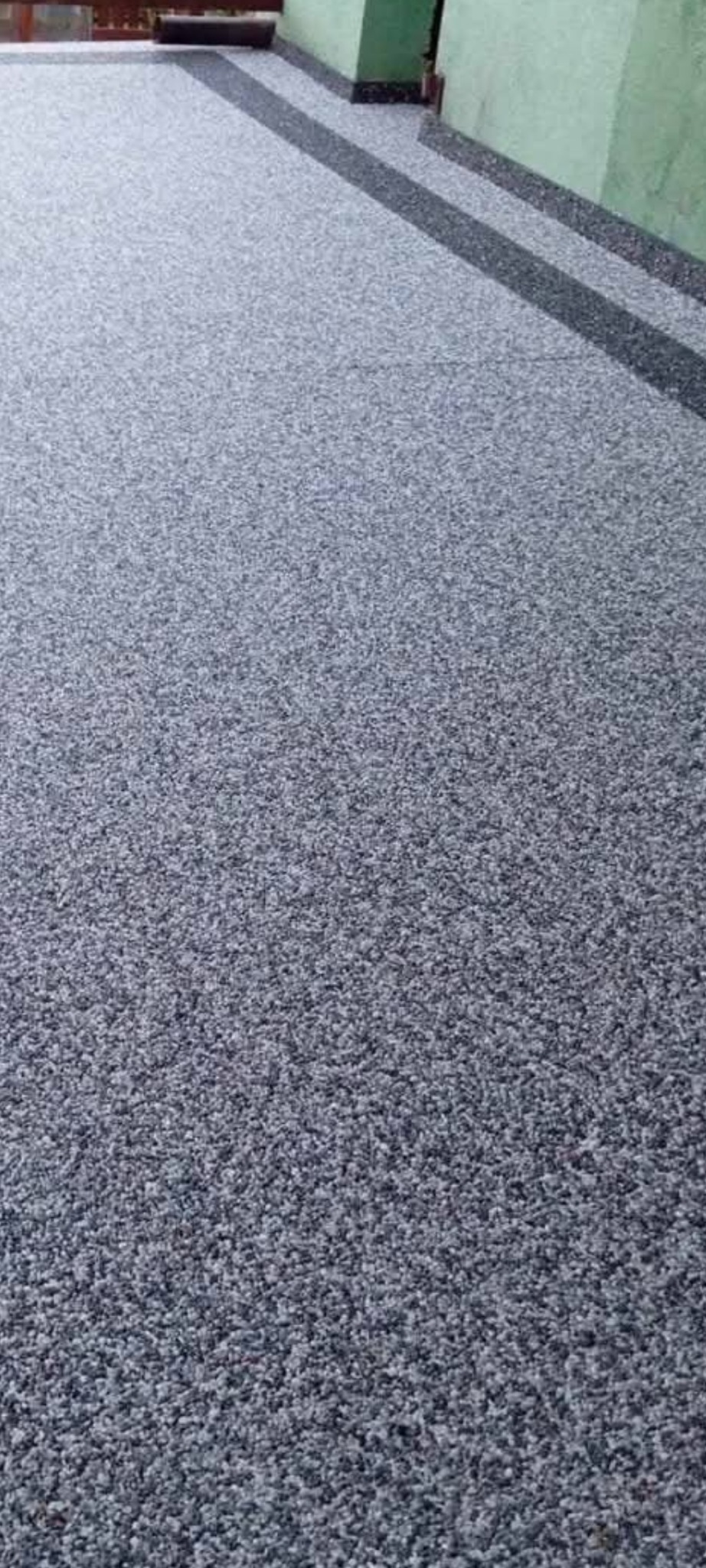 Szara posadzka żywiczna na zewnątrz budynku, z ciemniejszymi pasami przy ścianie. Jednolita tekstura, neutralne kolory, widok z góry.