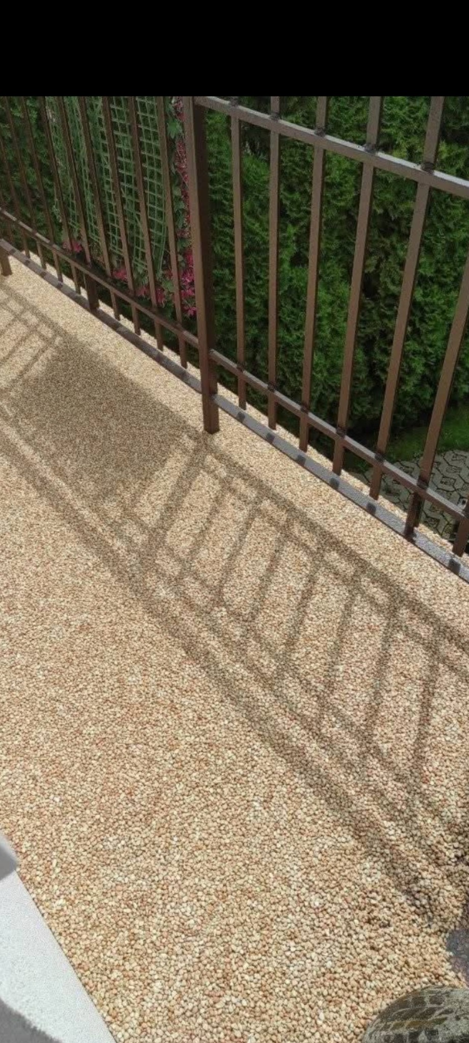 Beżowa posadzka żywiczna na balkonie w Woli. Widoczne cienie metalowej balustrady i zieleń w tle. Delikatna faktura nawierzchni.
