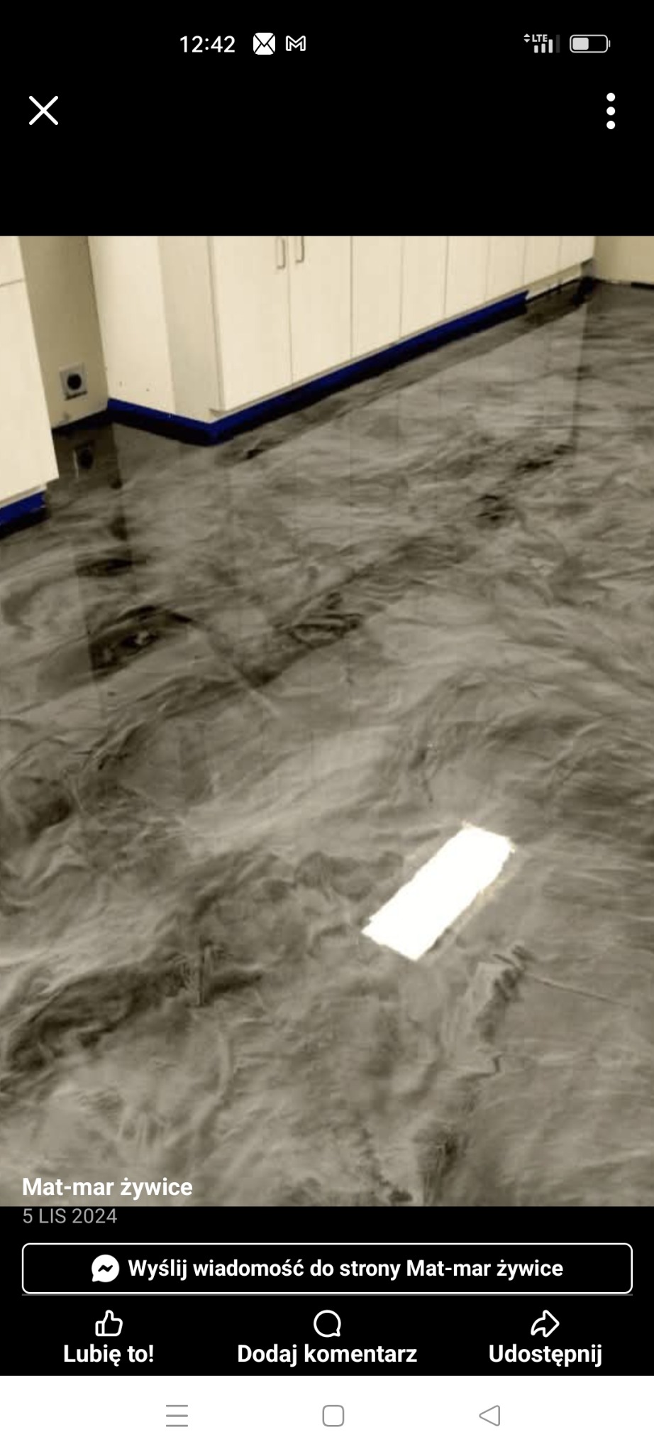 Błyszcząca, szara posadzka żywiczna z efektem marmuru, wykończona niebieską listwą przypodłogową, pod białymi szafkami. Widok z góry, oświetlenie odbija się od gładkiej powierzchni.