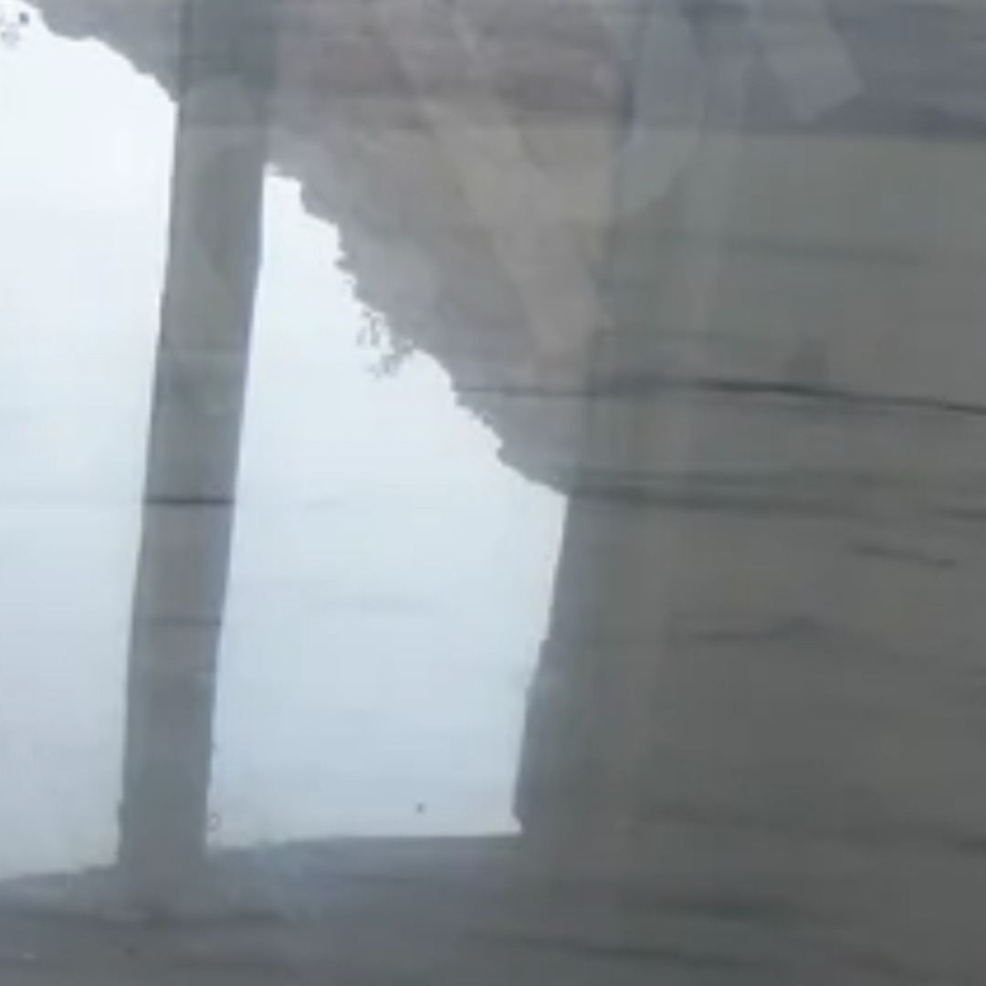 Nietypowe ujęcie skalnej ściany z roślinnością, widzianej przez szklaną powierzchnię z refleksami, tworzące abstrakcyjny, zamglony krajobraz.