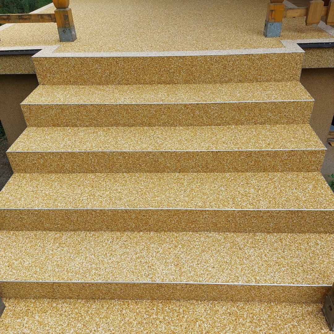 Złociste schody zewnętrzne z żywicy epoksydowej, wykończone srebrną listwą, prowadzące na taras. Widok z dołu, oświetlenie naturalne.