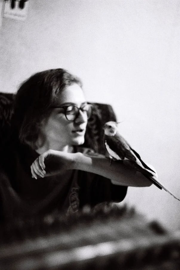 Czarno-białe zdjęcie kobiety w okularach z nimfą na ramieniu, patrzącej w dół.