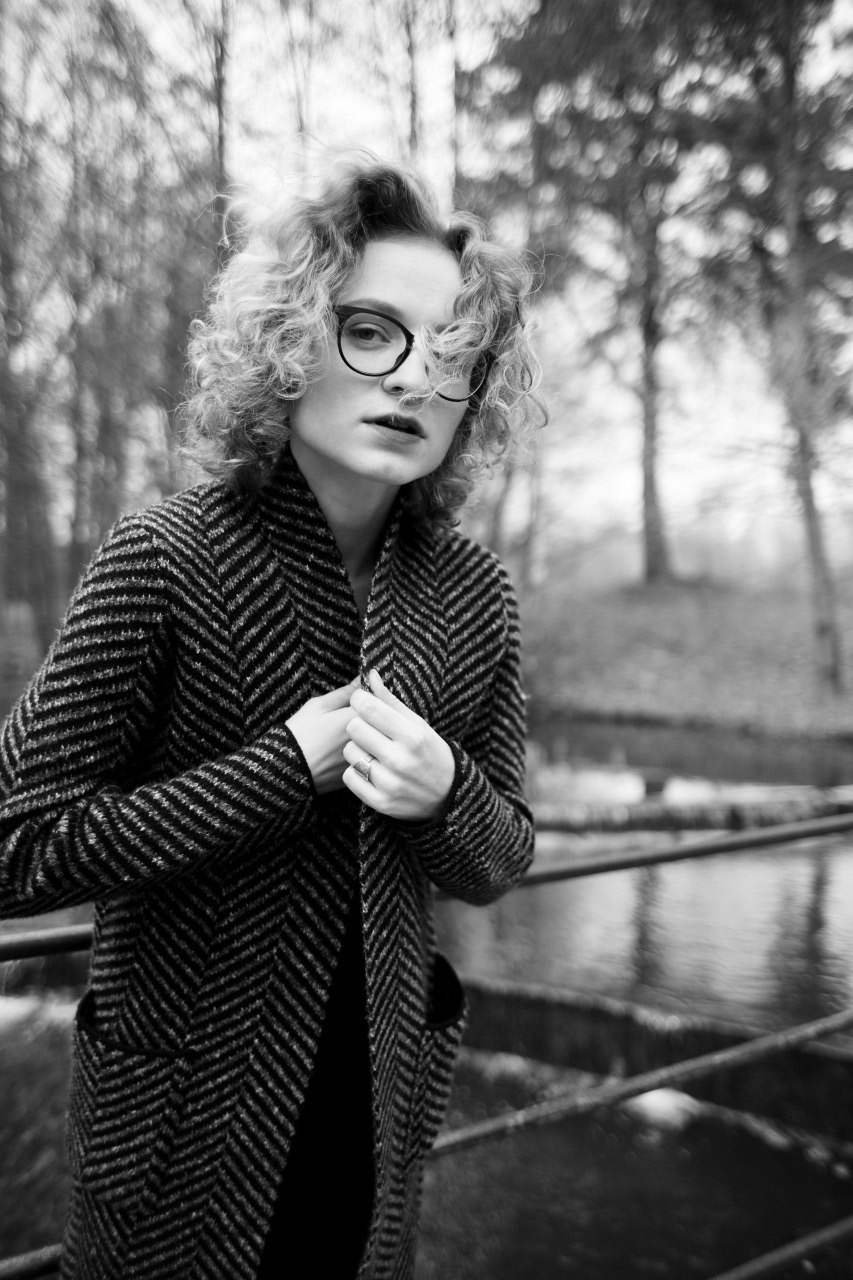 Portret kobiety w okularach i płaszczu w jodełkę na tle parku we Wrocławiu, czarno-białe zdjęcie z lekkim rozmytym tłem.