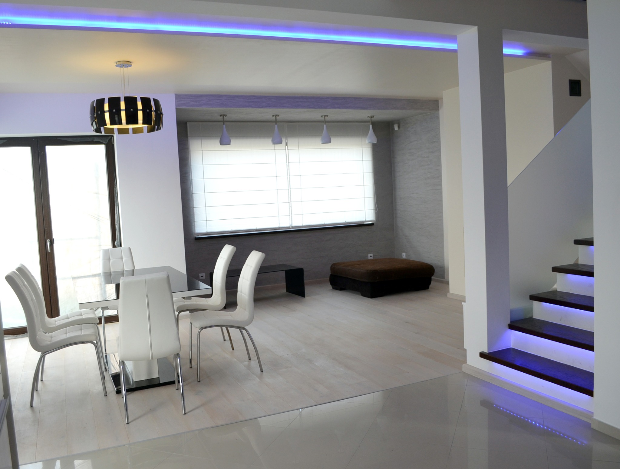 Nowoczesne wnętrze w Warszawie z białymi krzesłami przy szklanym stole, podświetlane schody i listwy LED w suficie.