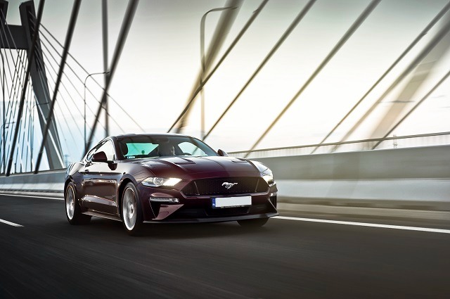 Bordowy Ford Mustang pędzi po moście pod światło, widoczne rozmycie ruchu.