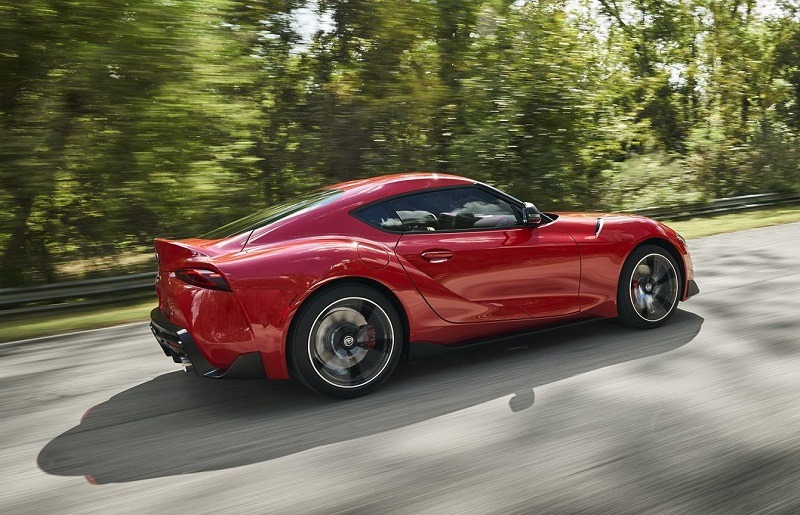 Czerwone sportowe auto na szosie w ruchu, widok z tyłu, z rozmazanym tłem drzew.