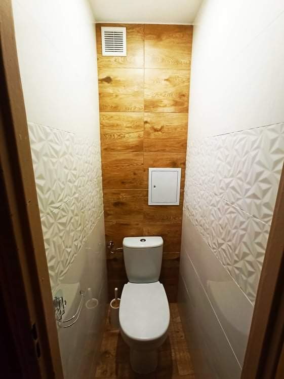 Wąska toaleta po remoncie z płytkami imitującymi drewno na ścianie, białymi płytkami 3D i nową armaturą.