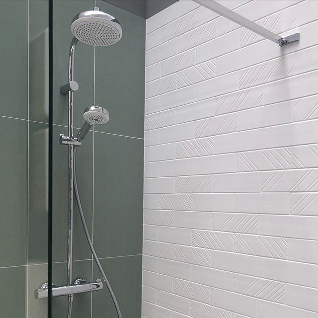 Nowoczesna kabina prysznicowa z deszczownicą i baterią termostatyczną, wykończona zielonymi i białymi płytkami z subtelnym wzorem.