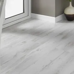 Jasnoszara podłoga z paneli laminowanych ułożona w pokoju, widoczny fragment białego krzesła i okna, dekoracyjna waza w rogu.