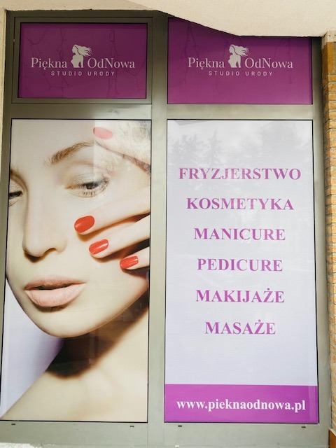 Witryna salonu urody Piekna OdNowa z plakatem prezentującym usługi: fryzjerstwo, kosmetyka, manicure, pedicure, makijaże i masaże. Na plakacie widoczna twarz kobiety z czerwonym manicure.