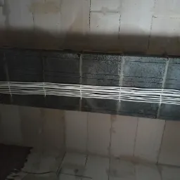 Białe przewody elektryczne ułożone poziomo wzdłuż szarej ściany z betonowych bloczków, częściowo w trakcie prac.