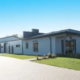 Budynek firmy z bramami przemysłowymi i konstrukcjami stalowymi, widok z zewnątrz, jasny dzień, kostka brukowa na podjeździe.